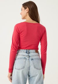 Top rojo de manga larga con escote redondeado, combinado con jeans de mezclilla azul claro de tiro alto con diseño estándar de bolsillos.