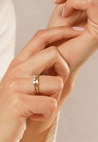 Gold- und Silberring an einem Finger, der drei kleine runde Diamanten zeigt. Die Hand hat einen hellen Hautton mit gepflegten Nägeln.