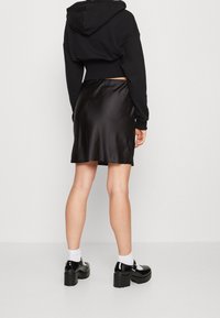 Sudadera negra corta con capucha, combinada con una falda de satén negro que tiene una textura suave y un dobladillo acampanado, llevada con zapatos de plataforma negros.