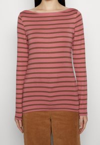 Långärmad, rosa skjorta med horisontella bruna ränder, som har en bred båthals. Matchas med bruna sammetbyxor, där den texturerade tyget är synligt.