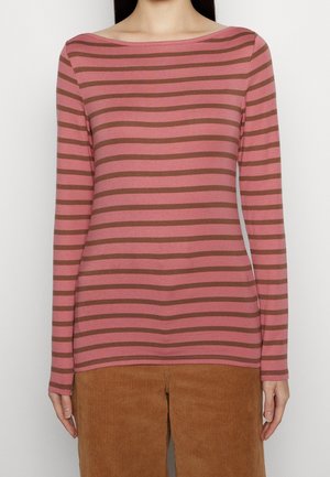 Lange mouwen, roze shirt met horizontale bruine strepen, voorzien van een brede bootnek. Gecombineerd met bruine corduroybroeken, textuur zichtbaar.