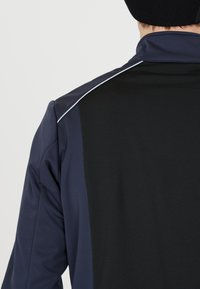 Marine- und schwarze Sportjacke mit taillierter Passform, hoher Kragen und reflektierenden Akzenten an den Schulternähten. Glatte Textur.
