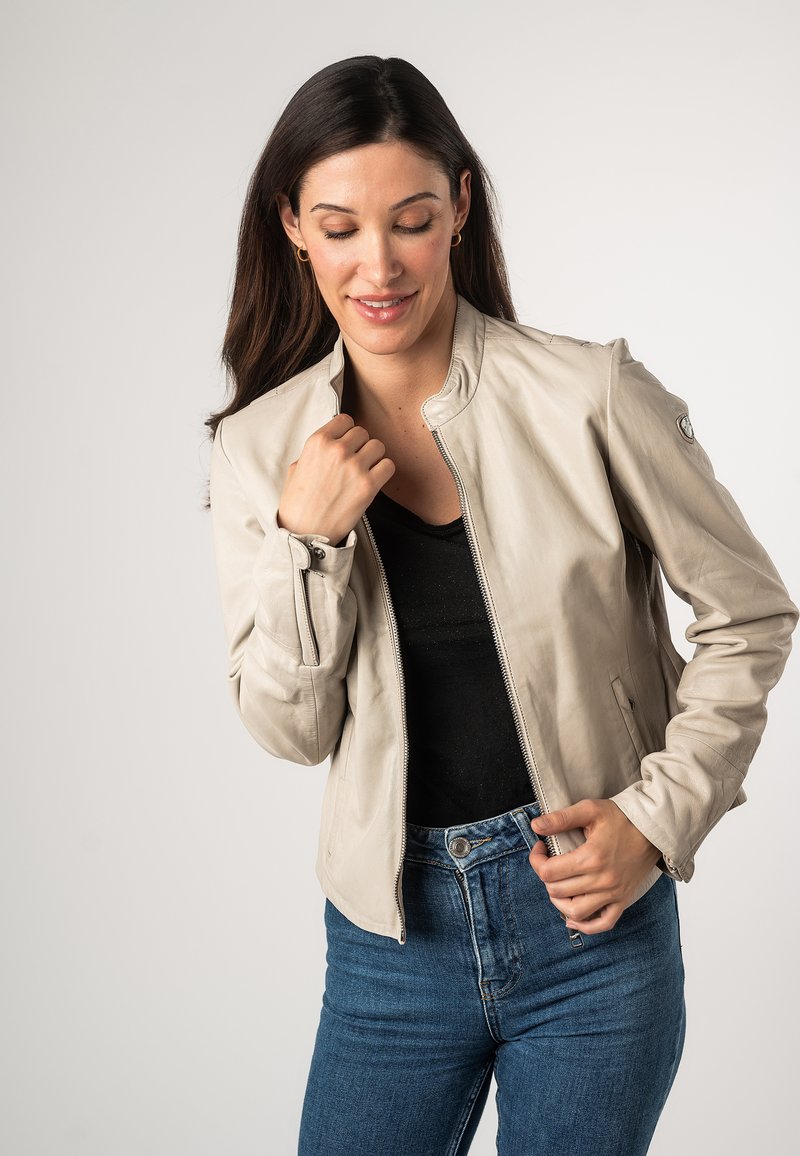 Lichtgekleurde leren jas met een ritssluiting, staande kraag en geribde boorden. Draagt over een zwart topje, gecombineerd met blauwe spijkerbroek.