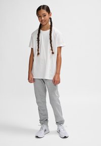 Weißes Baumwoll-T-Shirt mit kurzen Ärmeln, kombiniert mit hellgrauen Sweatpants und weißen Sportschuhen. Haare in zwei Zöpfen frisiert.