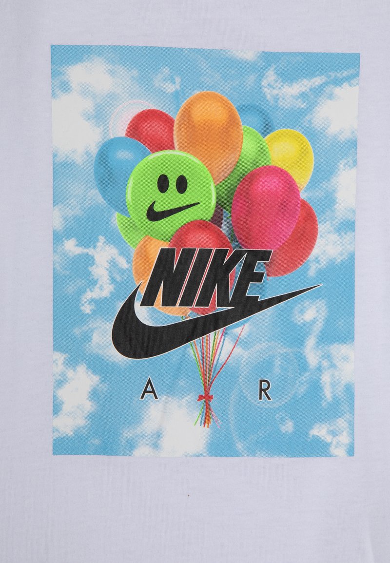 Witte T-shirt met een levendige grafiek van ballonnen in verschillende kleuren, een groene glimlachende gezicht en een opvallend zwart Nike-logo met kleurrijke strengen.
