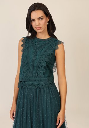 Teal lace dress with scalloped edges, intricate floral patterns, and a fitted bodice transitioning to a flowing polka dot skirt.