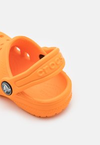 Fényes narancssárga Crocs szandál, amely könnyű műanyagból készült, szellőző résekkel, hátsó pánttal és dombornyomott márkaneves részlettel rendelkezik.