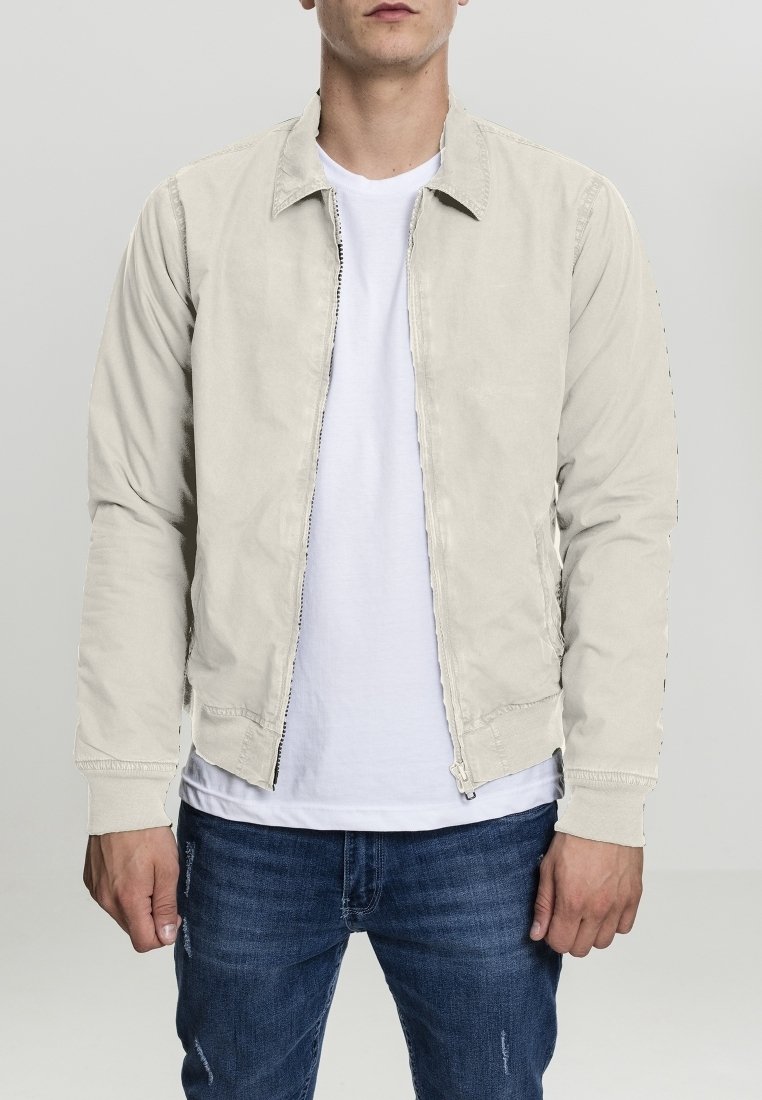 Beige leichte Jacke mit Reißverschluss vorne, spitzem Kragen und Seitentaschen, getragen über einem weißen T-Shirt und blauen Jeans.