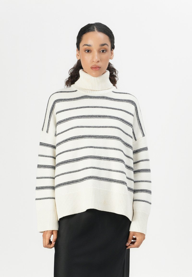 Weiß gestreifter Rollkragenpullover mit horizontalen schwarzen Streifen, gerippten Bündchen und einem lockeren, entspannten Schnitt. Tragen über einem schwarzen Rock.
