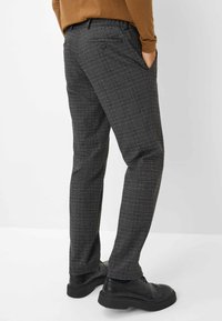 Pantaloni a quadri grigi con una vestibilità slim, dotati di una tasca posteriore con bottone e una texture liscia, abbinati a scarpe nere.