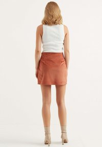 Roestkleurige corduroy mini-jurk met een gladde textuur en twee achterzakken, gecombineerd met een aansluitend wit geribbeld tanktop.