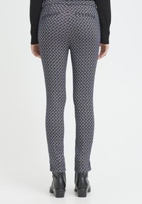 Schmal zulaufende Leggings mit einem geometrischen Muster in Marineblau und Gold, gefertigt aus einem elastischen Stoff, kombiniert mit schwarzen Stiefeletten.