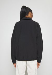 Černá bunda s klasickým límcem a elastickým lemem. Materiál je hladký a lehký, vhodný pro volnočasové nošení.