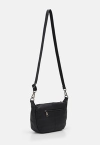 Sac à épaule en cuir noir avec une seule sangle réglable, compartiment principal zippé et poche avant. Texture lisse et design minimaliste.