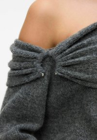 Grauer, schulterfreier Pullover aus strukturiertem, weichem Strickstoff. Mit Fältchen und zwei silbernen Akzenten in der Mitte.