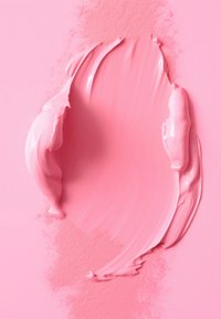 Rosa grädde utspridd på en platt rosa yta, med en texturerad, glänsande yta. Ljusrosa pulverstänk ligger utspridda i närheten och ger kontrast.