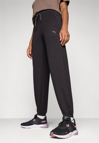 Svarta sweatpants med dragsko i midjan och fickor, prydda med en liten silverlogga på vänster sida, i kombination med svarta träningsskor.