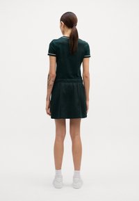 Vestido polo verde con ribetes blancos y una cintura elástica, con una falda acampanada. El material parece suave. Combinado con calzado blanco.