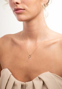 Gouden ketting met een ronde hanger en een klein sterretje eraan. De ketting is fijn en complementeert de halslijn van een lichtgekleurde top.