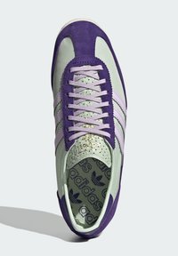 Svetlozelené a fialové tenisky vyrobené zo zamate a sieťoviny, s tromi pruhmi, perforovanými detailmi a vzorovanou vnútornou stielkou.