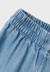 Tessuto in denim blu chiaro con una vita elastica arricciata. La superficie è liscia con cuciture e dettagli di cucitura visibili.