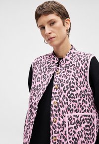 Ροζ κολαριστό γιλέκο με μαύρο λεοπάρ σχέδιο, διαθέτοντας ψηλό γιακά, κουμπιά μπροστά και μία τσέπη. Υφή υφάσματος, άνετος σχεδιασμός.