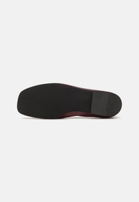 Svart gummisåle med en jevn tekstur. Liten buet form, med en bordeauxfarget hæl og flat design.