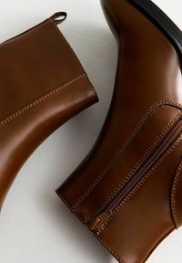 Bottes chelsea en cuir brun avec une texture lisse, des fermetures éclair sur le côté et des coutures contrastées. Présentent une languette et un design à bout arrondi.