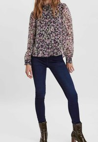 Kukallinen pusero, jossa on liehukehihat, violetein ja vihrein sävyin; yhdistetty tummansinisiin kapealahkeisiin farkkuihin ja tummiin nilkkureihin.