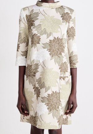 Sukienka w kwiatowy wzór w kolorze beżowym, z zielonymi i brązowymi kwiatami. Rękawy do łokcia i wysoki kołnierz. Dwie boczne kieszenie.