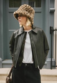 Black leather zip-up jacket with a pointed collar over a white shirt, paired with a leopard print faux fur bucket hat and black skirt.