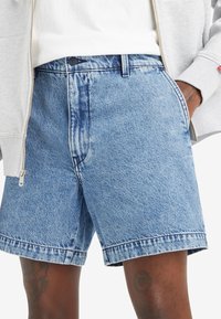 Jeanși scurți de culoare albastră deschisă, cu o croială largă, având un sistem de închidere cu buton, buzunare frontale și tiv brut. Dacără clasica din denim texturat.