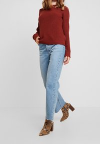 Un pull côtelé couleur rouille associé à un jean droit bleu clair et des bottines beige à motifs serpent avec un talon épais.