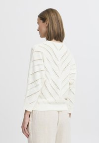 Weißer Strickpullover mit Zickzackmuster und Öffnungsdetails. Verfügt über Dreiviertelärmel und gerippten Saum. Texturiertes, gewebtes Material.