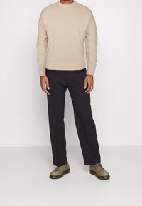 Pull en tricot beige avec un col rond, assorti à un pantalon bleu marine foncé et des chaussures en cuir tan. Design simple et silhouette ajustée.