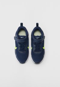 Baskets de sport en maille navy avec accents jaune fluo, une sangle à boucle et une semelle blanche. Elles présentent un col rembourré pour plus de confort.