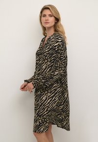 Abito lungo in stampa animale nera e beige con colletto, maniche ampie e orlo fino al ginocchio. Il tessuto ha una texture liscia.
