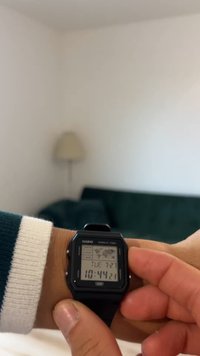 Casio skaitmeninis laikrodis su juodos spalvos plastikiniu korpusu ir dirželiu; šviesiai pilkas LCD ekranas, rodantis laiką (10:44), datą ir pasaulio žemėlapio grafiką.