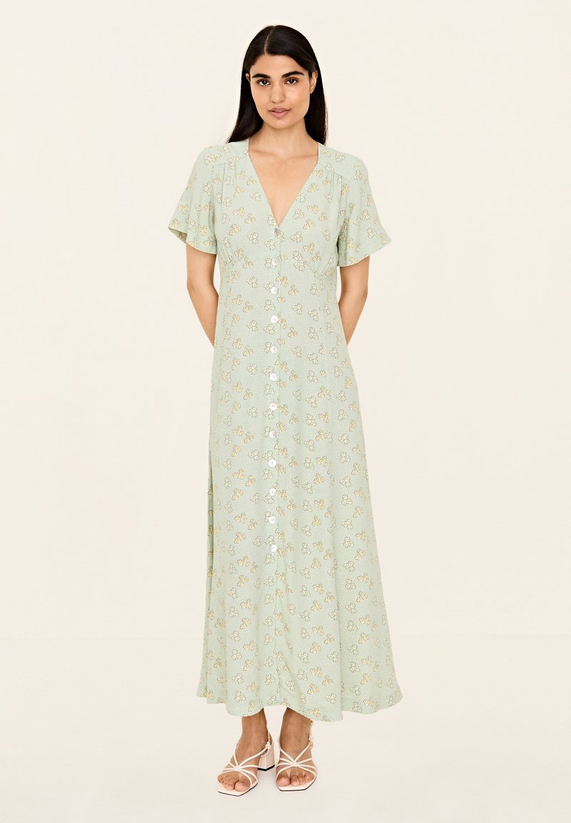 Hellgrünes, knielanges Kleid mit Blumendruck, V-Ausschnitt, kurzen Ärmeln, Knopfverschluss vorne und einem schwingenden Design. Akzentuiert mit weißen Knöpfen.