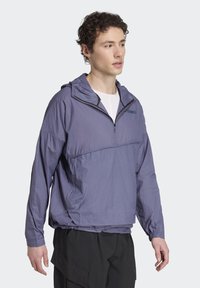Lightweight purple pullover jacket with a half-zip design, hood, and elastic cuffs. Features a textured fabric and a chest logo. Black accents included.