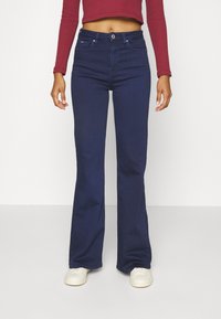 Tummansininen leveälahkeinen farkkuhousut, jotka on valmistettu denimistä ja joissa on nappikiinnitys, vyölenkit, kaksi etutaskua ja sileä pinta.