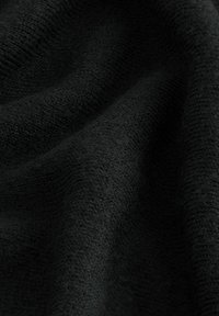 Gros plan sur un tissu tricoté noir doux et texturé avec un tissage visible et des plis créant des ombres et de la profondeur.