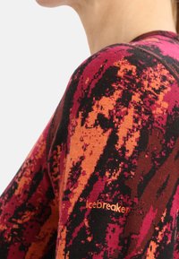 Villapusero, jossa on eloisat punaisen, oranssin ja mustan abstraktit kuviot. Hihassa pieni oranssi "Icebreaker"-logo.