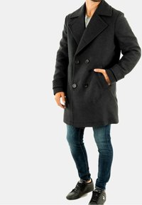 Abrigo pea de lana negra con botones dobles, grandes solapas y bolsillos laterales, combinado con vaqueros azules y zapatillas negras.