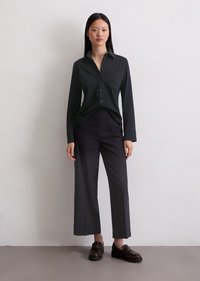 Camicia nera a maniche lunghe con taschino sul petto, abbinata a pantaloni scuri a vita alta. Tessuto testurizzato e vestibilità ampia per il massimo comfort. Scarpe basse completano il look.