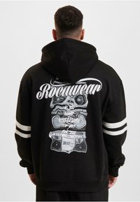 Svart hettegenser med hvit grafisk tekst og en boombox-design på baksiden, med hvite striper på ermene.