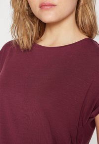 Vínové tričko s krátkými rukávy a širokým výstřihem z hladké, měkké tkaniny. Textura působí lehce a přiléhavě kolem trupu.