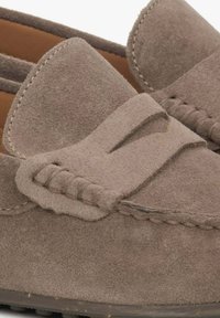Brązowe zamszowe loafersy z płaską podeszwą, z przeszyciem na wierzchu oraz szerokim, teksturowanym paskiem z przodu.