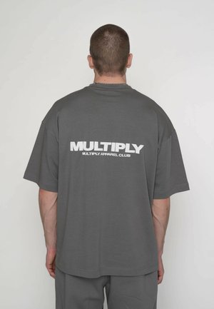 Tricou gri supradimensionat cu inscripția „MULTIPLY” imprimată alb pe spate. Design simplu, mâneci scurte și textură moale a țesăturii.
