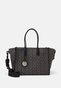Black and brown patterned tote bag with rounded handles, adjustable shoulder strap, and round gold logo charm hanging on front.